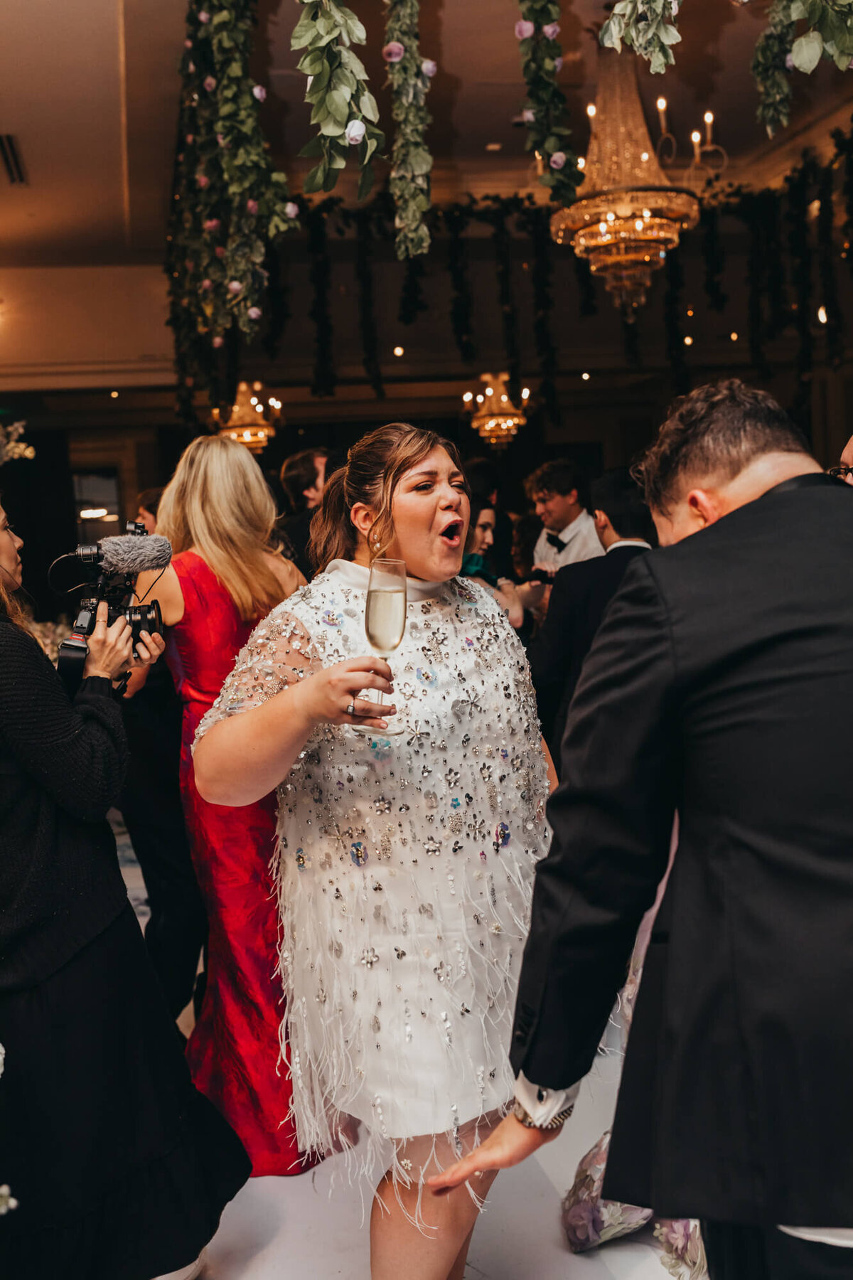brides hold champagne glass while dancing with her husband at the party.
