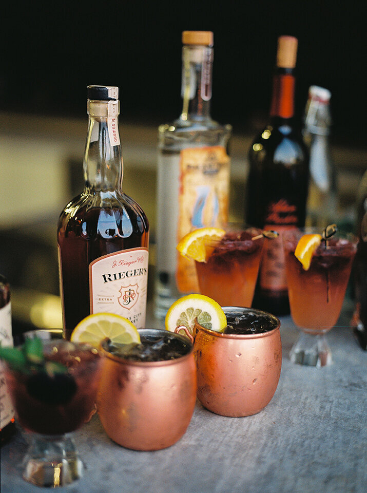 Rose gold mules with lemon wedges next to an assortment of cocktails and liquor bottles.