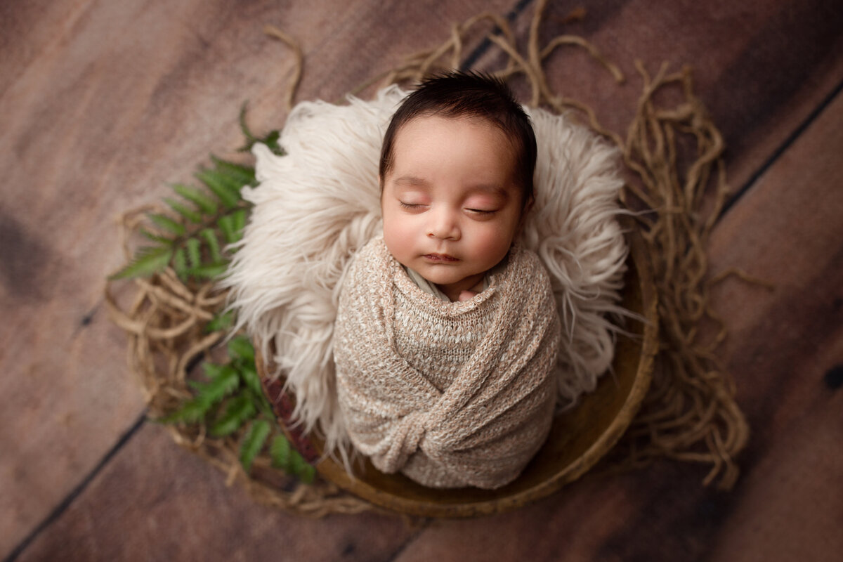 baby boy sleeping in a wooden bowl on a wood floor