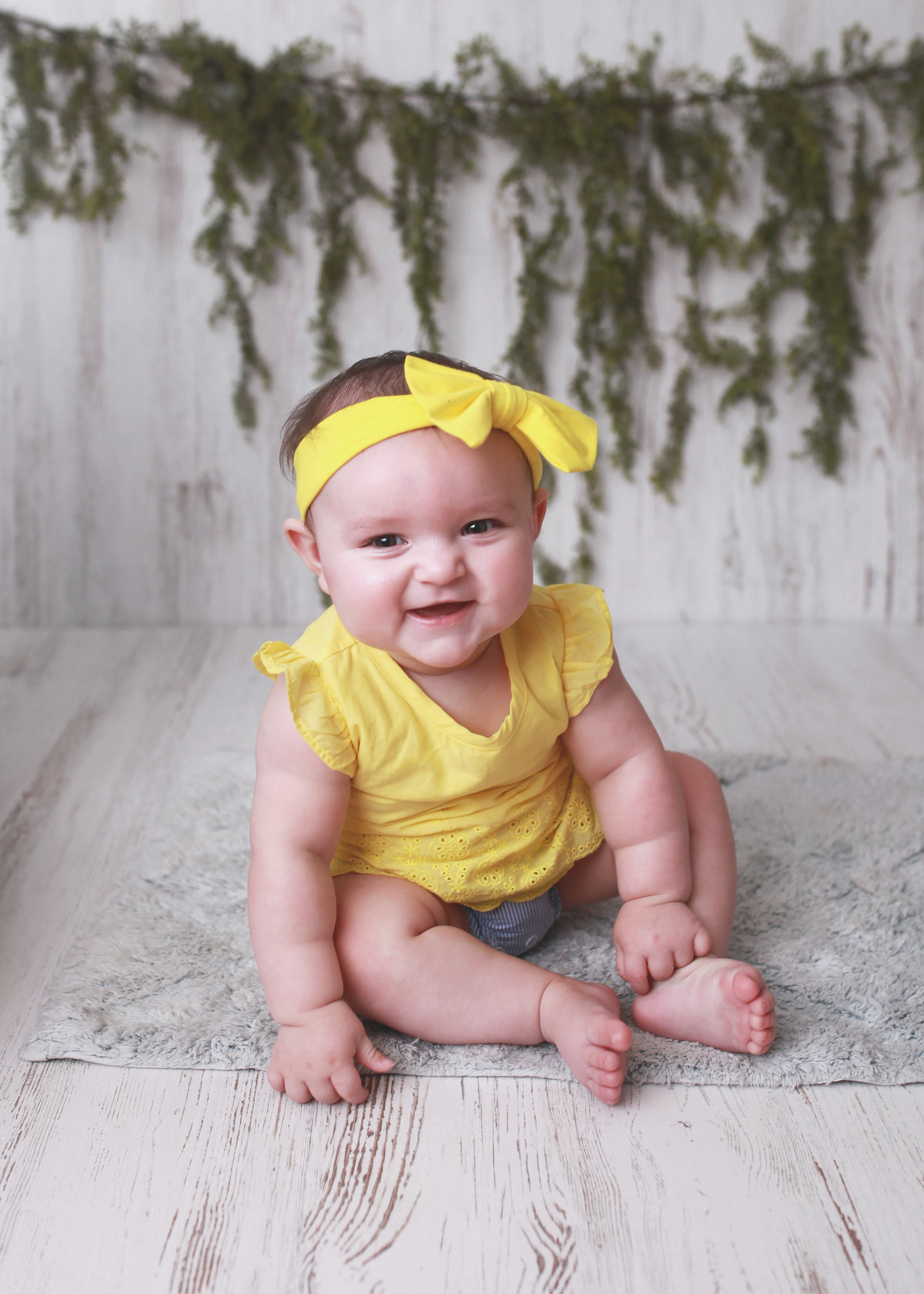 baby girl posed on floor with yellow shirt and matching bow on head
