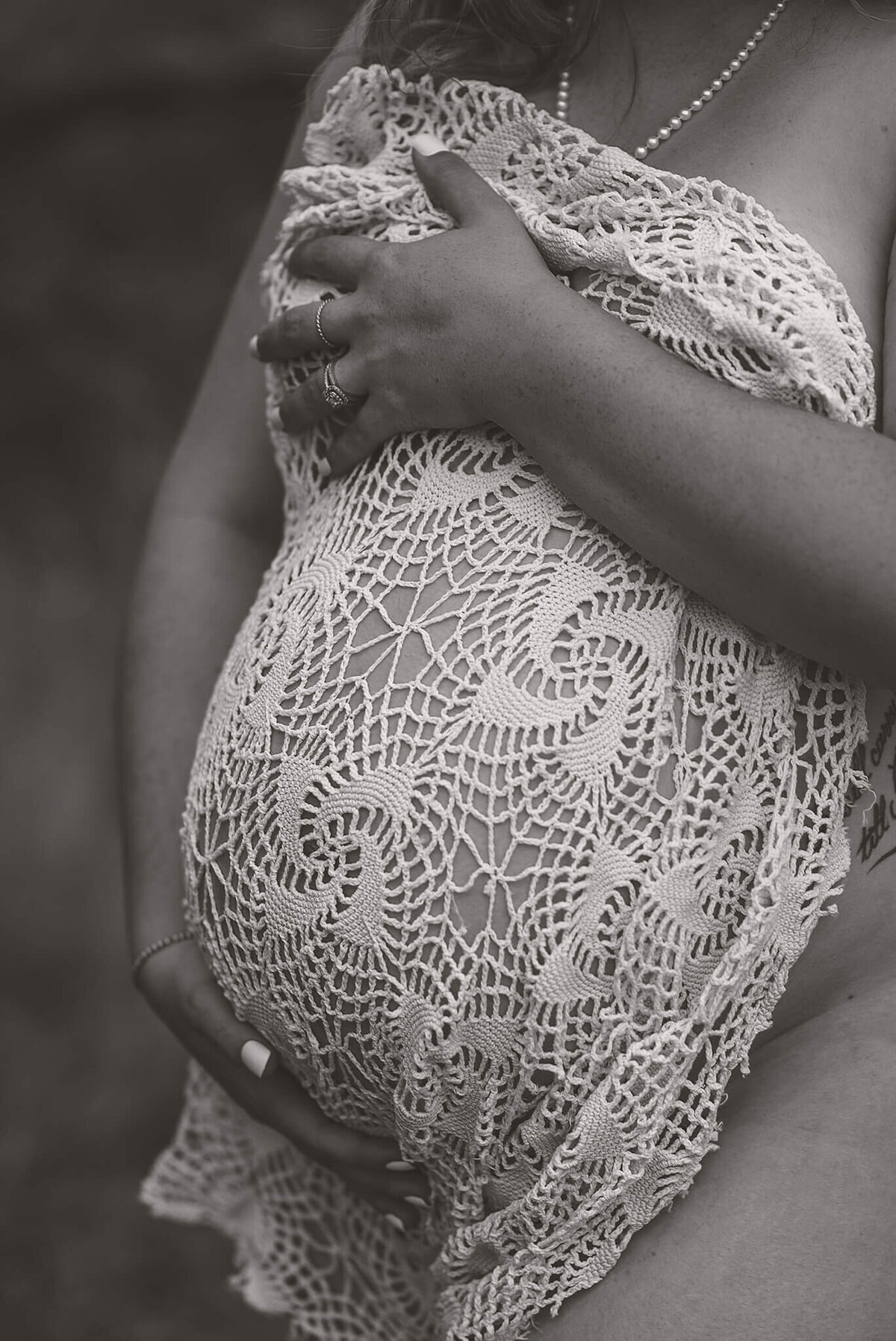 A black and white image of a pregnant belly with corcheted fabric covering her breasts and belly.