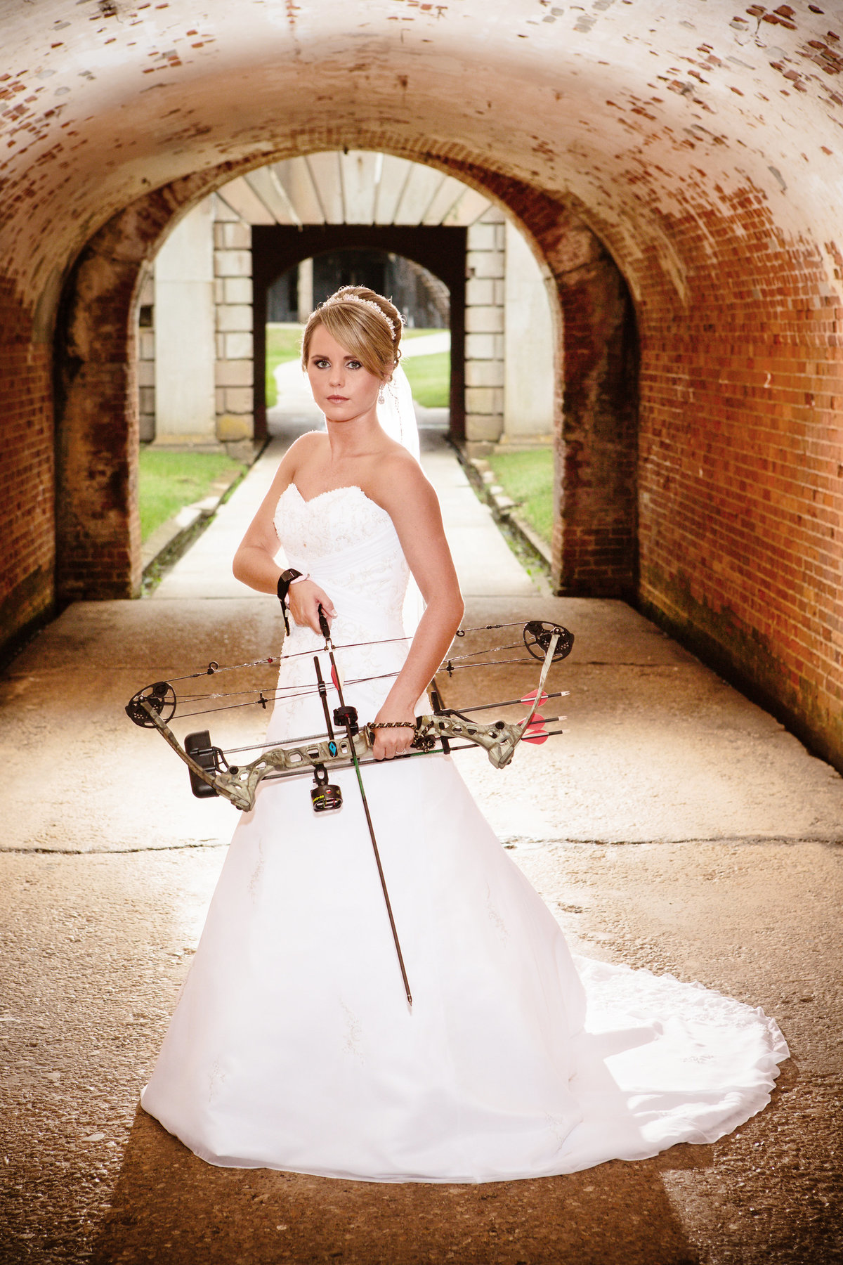 A bride who likes to hunt poses with her compound hunting bow in Fort Morgan, Alabama.