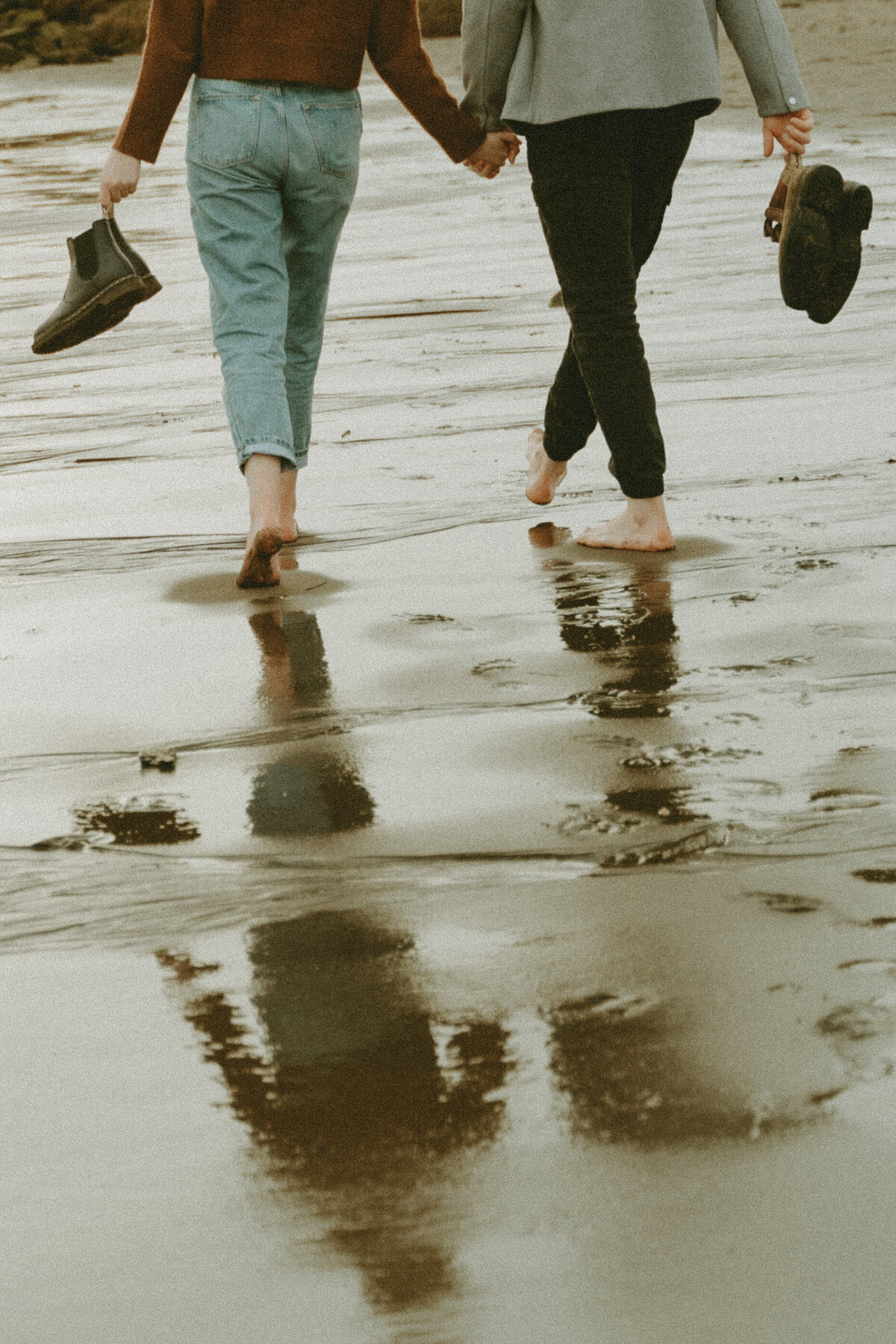 modern photo of a couple walking away on a beach holding their shoes in hands