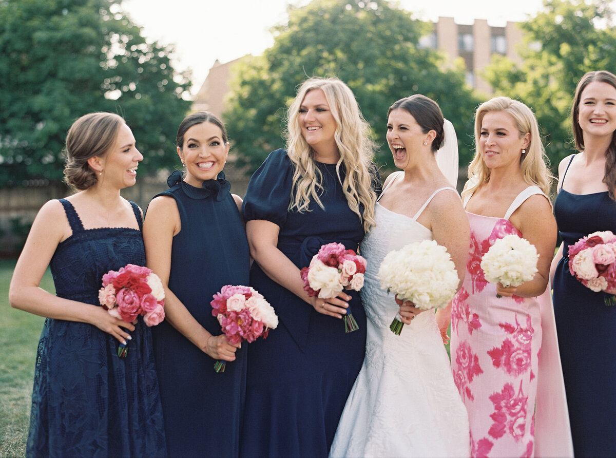 Bride laughing with bridesmaids in navy and floral dresses at Saddle Country Club.