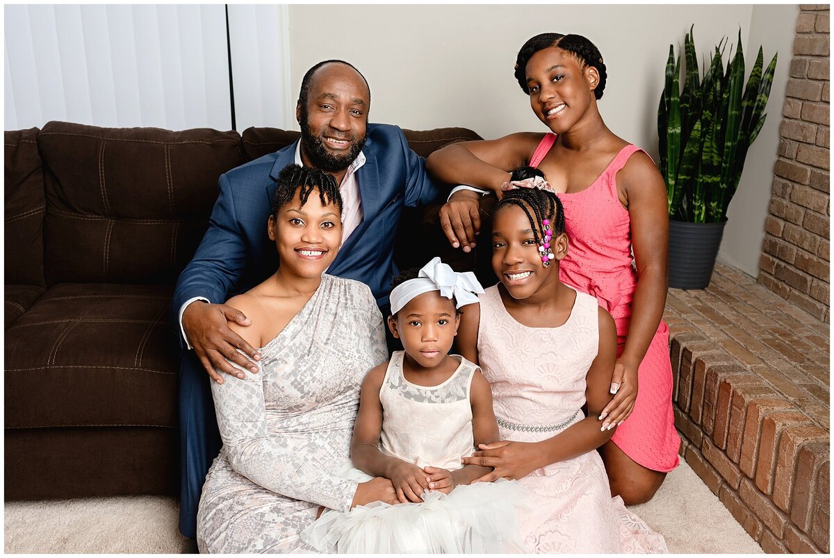 Parents and their children sitting in front of their couch in a tight-knit pose symbolizing thier strong bond and unity in their family portrait session.