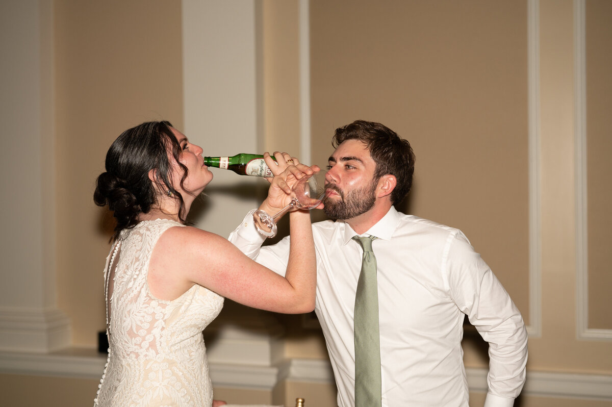 A newlywed couple with their arms linked as they both take a drink