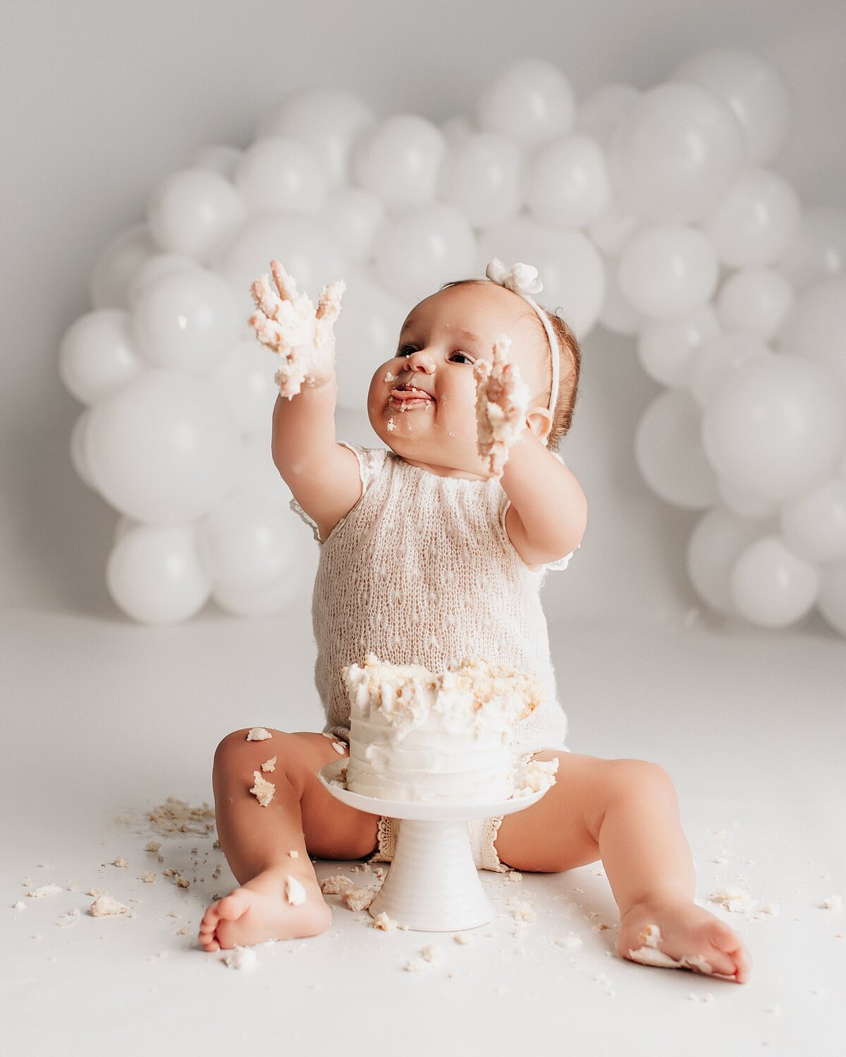 Baby smiling next to birthday cake during cake smash session