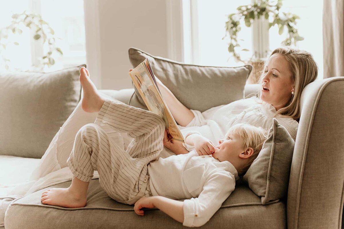 En mor og sønn ligger på safaen og leser en bok sammen under familiefotografering på Frogner i Oslo.