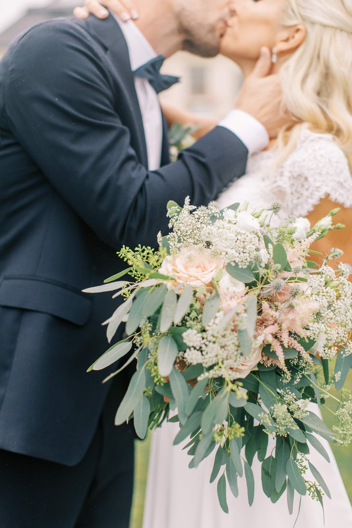 Bruden håller en pastellfärgad brudbukett och pussar sin man