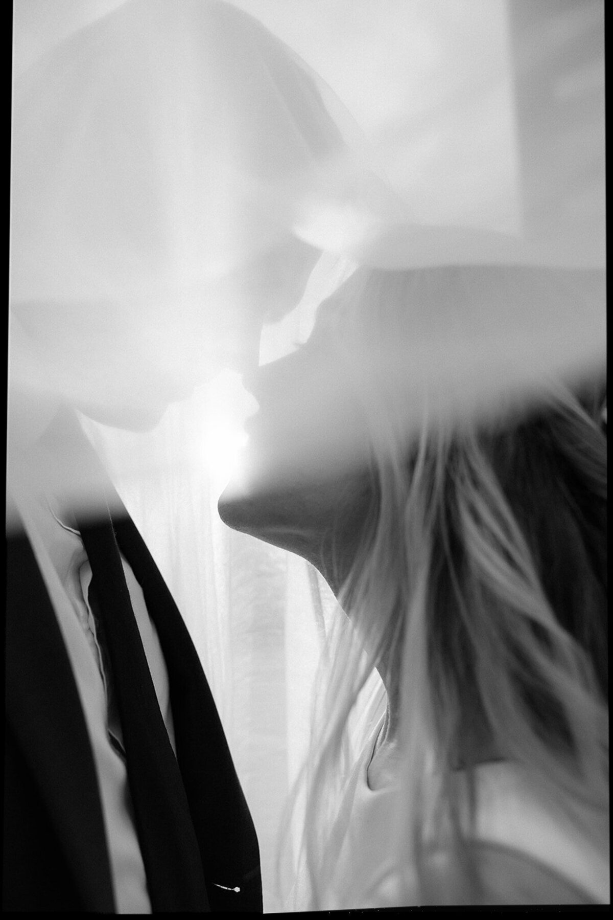 Newlywed couple go nose to nose under her veil shot in black and white on the east coast. 