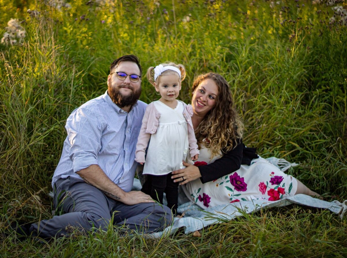 an Edmonton couple sits on a picnic blanket with their toddler daughter
