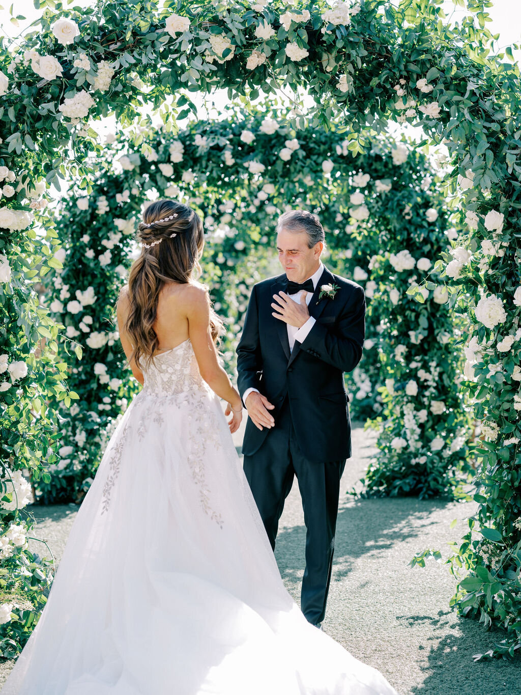 A touching moment as the father sees his daughter in her wedding gown for the first time, standing beneath a romantic floral arch in Scottsdale.