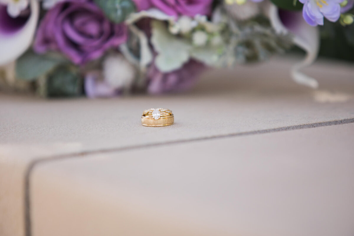 wedding rings in front of a purple bouquet