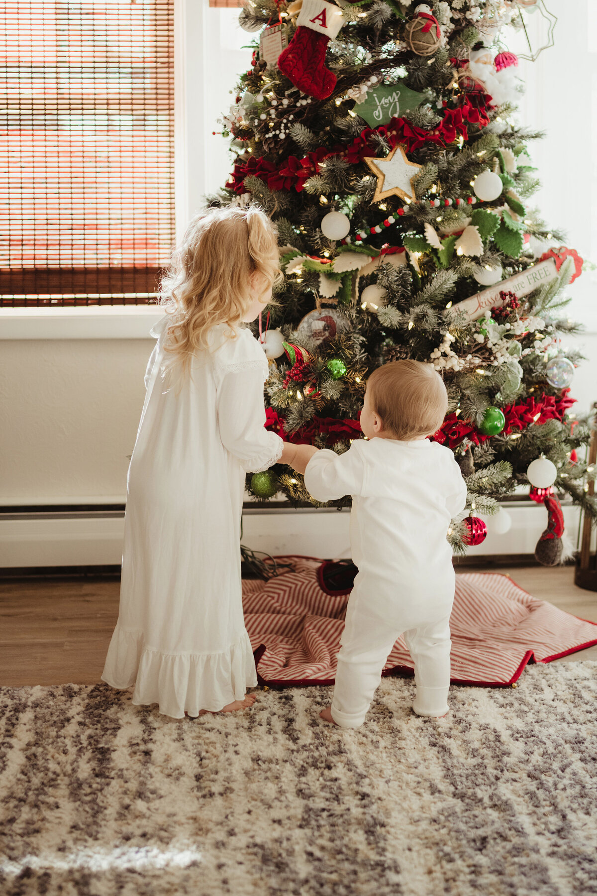 An older sister and little sister excitedly look at the Christmas tree.