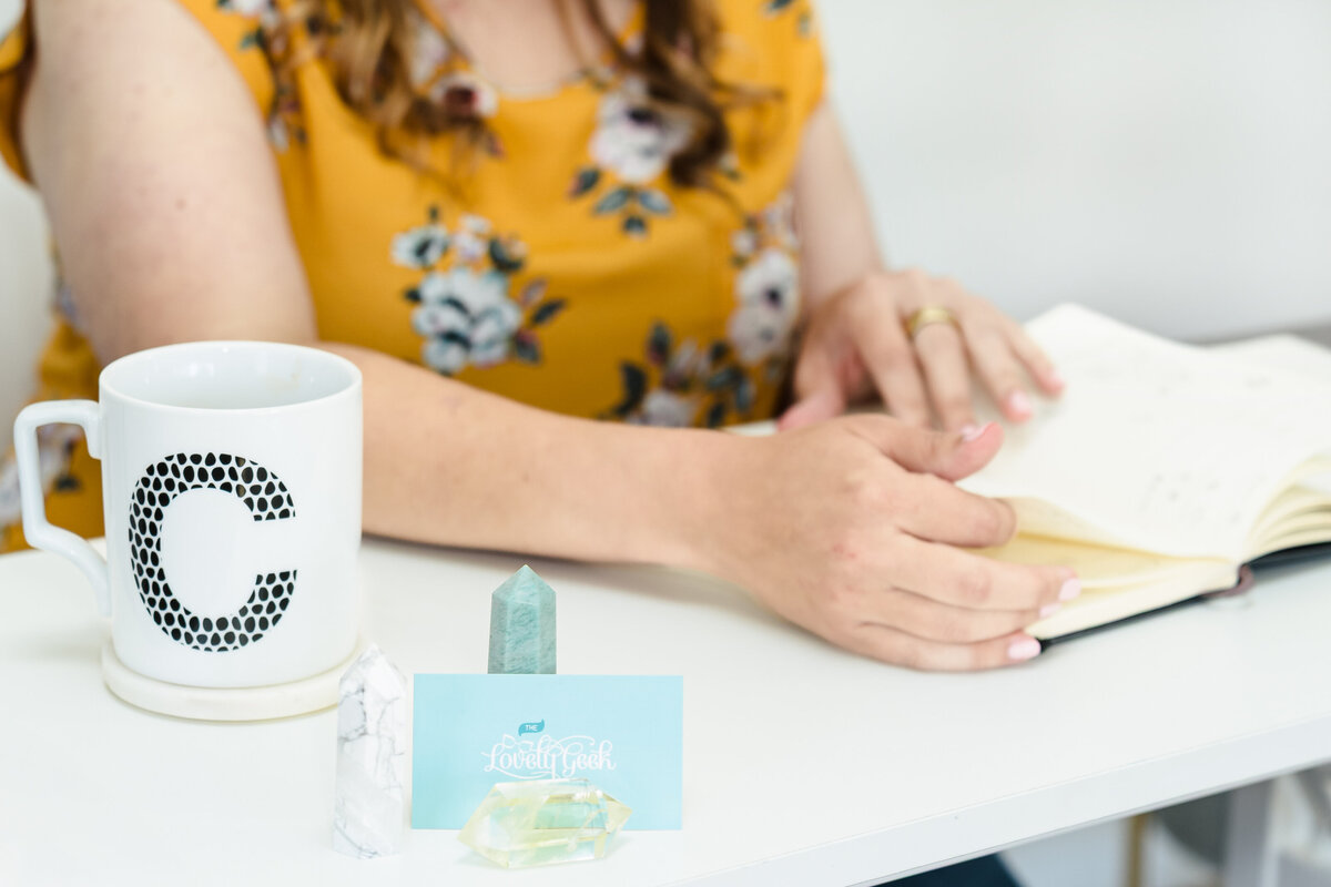 brand photo of a web designer showcasing her hands in a notebook, business card, and crystal on the desk as a foreground