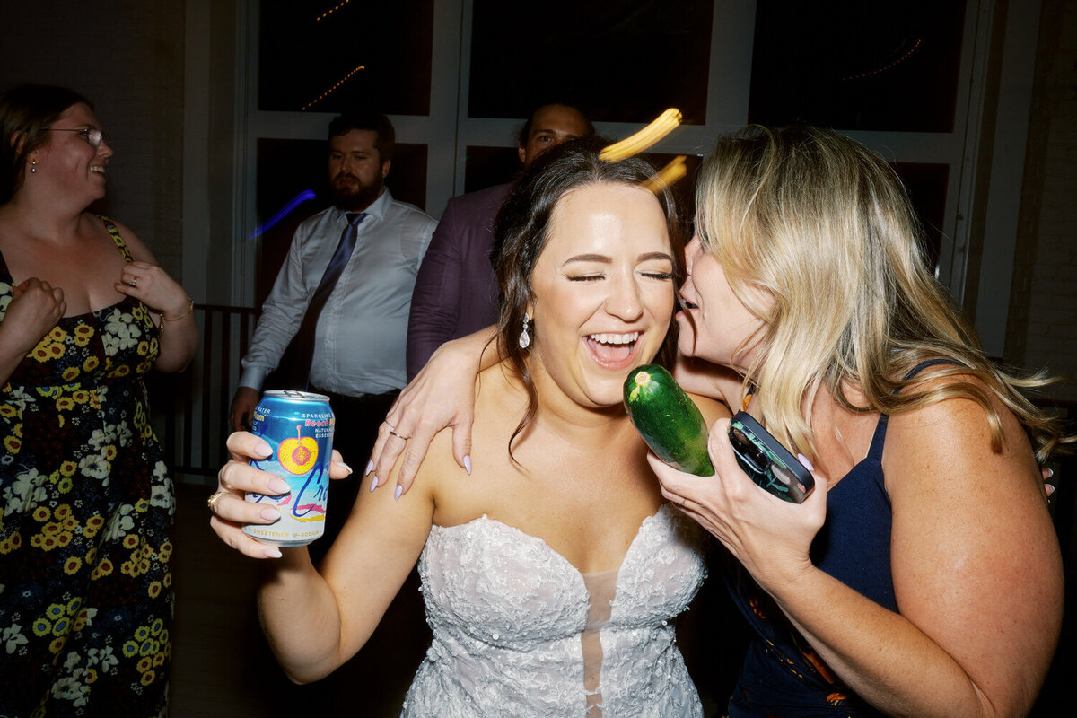 Bride laughing on the dance floor as her friend whispers in her ear