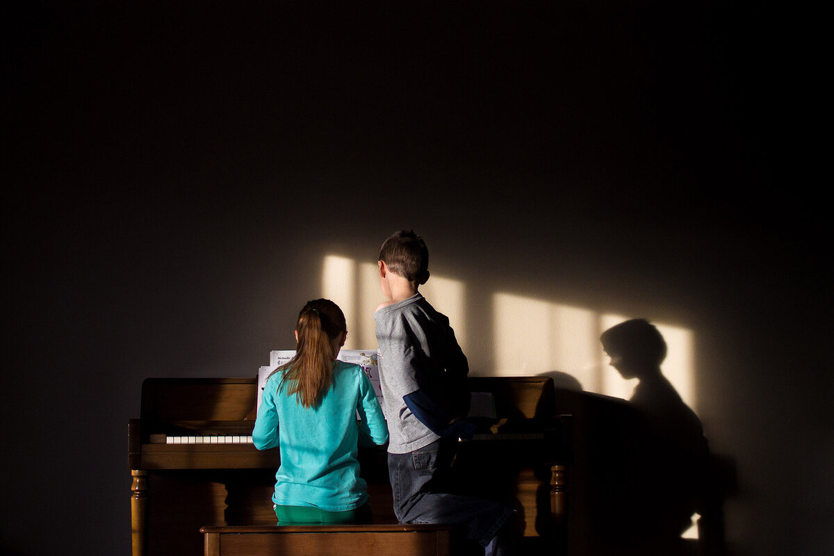 two siblings at the piano in window light and shadows