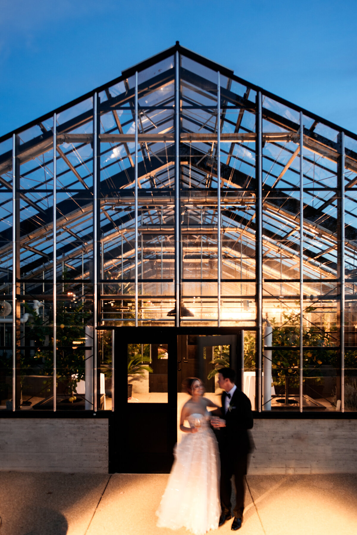 bride and groom standing outside a greenhouse at night at their wedding