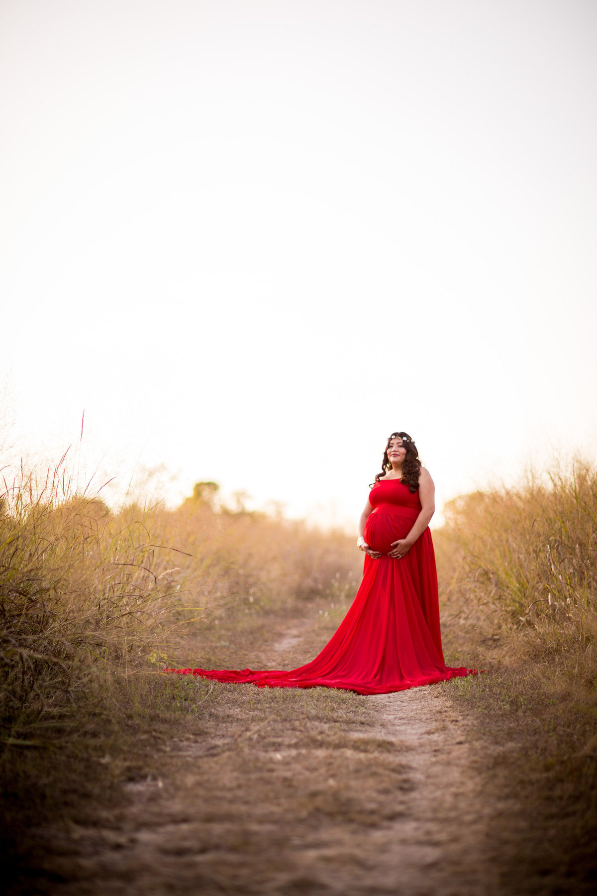 San Antonio Maternity photography session of woman in red maternity dress standing in field at Cibolo Nature Center.