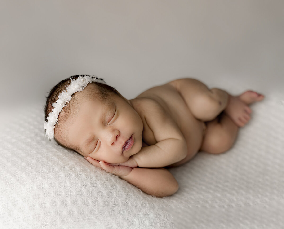 baby girl on white backdrop with her hands laying on her cheeks