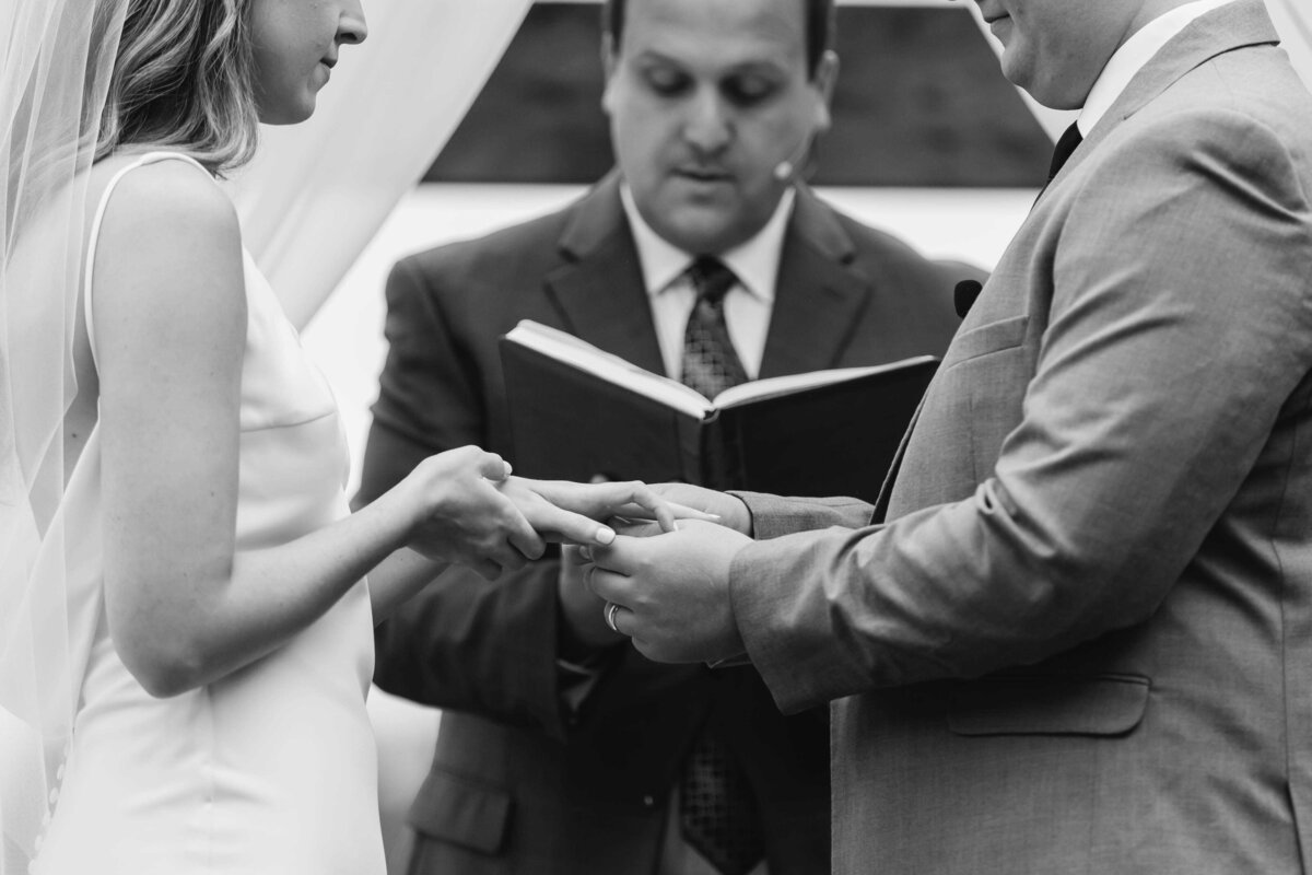 Bride and groom exchange rings with officiant in background