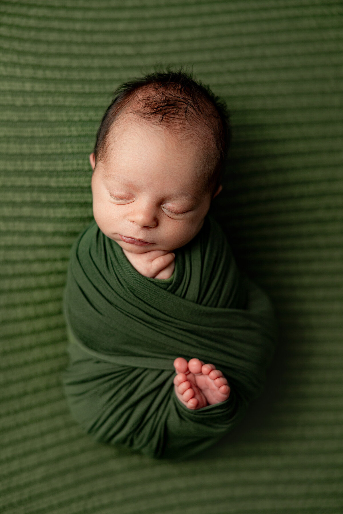 newborn baby wrapped with toes peaking out and sleeping for photo session in traverse city