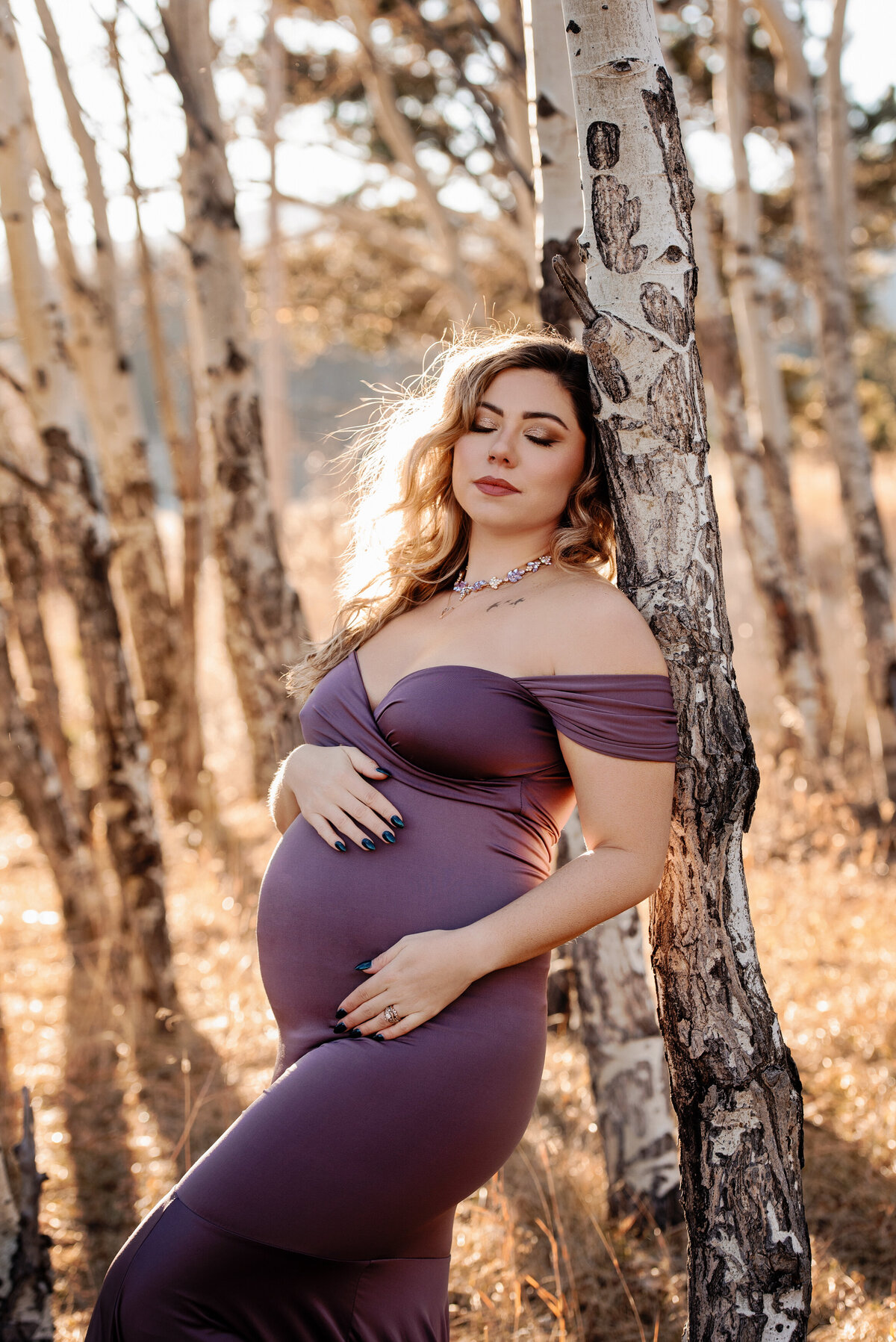 colorado-maternity-photographer-expecting-mom-in-purple-fitted-dress-leaning-on-birch-tree