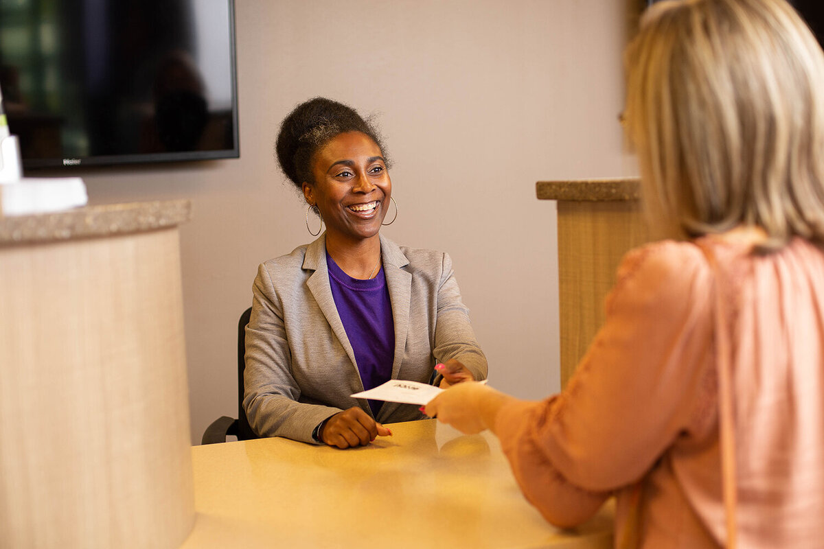 African-American female bank teller handing papers to a customer at a bank window