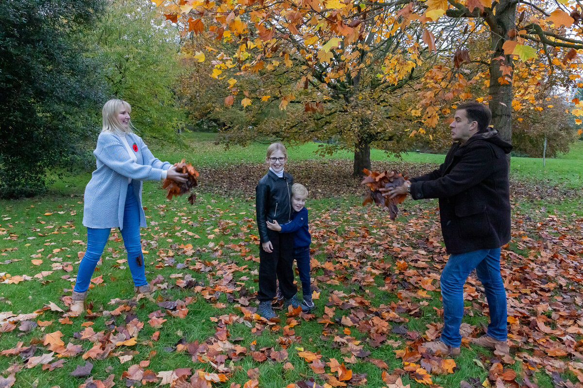 A family having a photography session playing with leaves in a park.