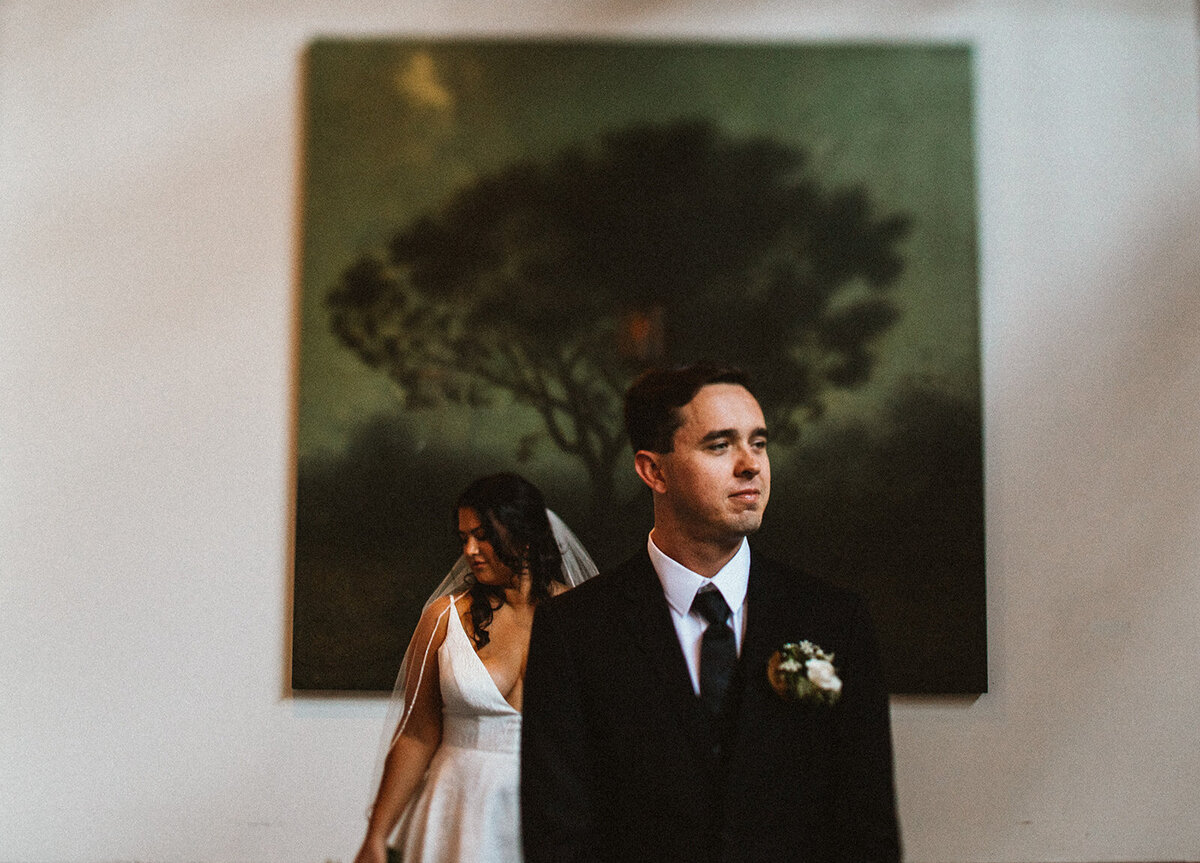 bride and groom stand in front of large painting 