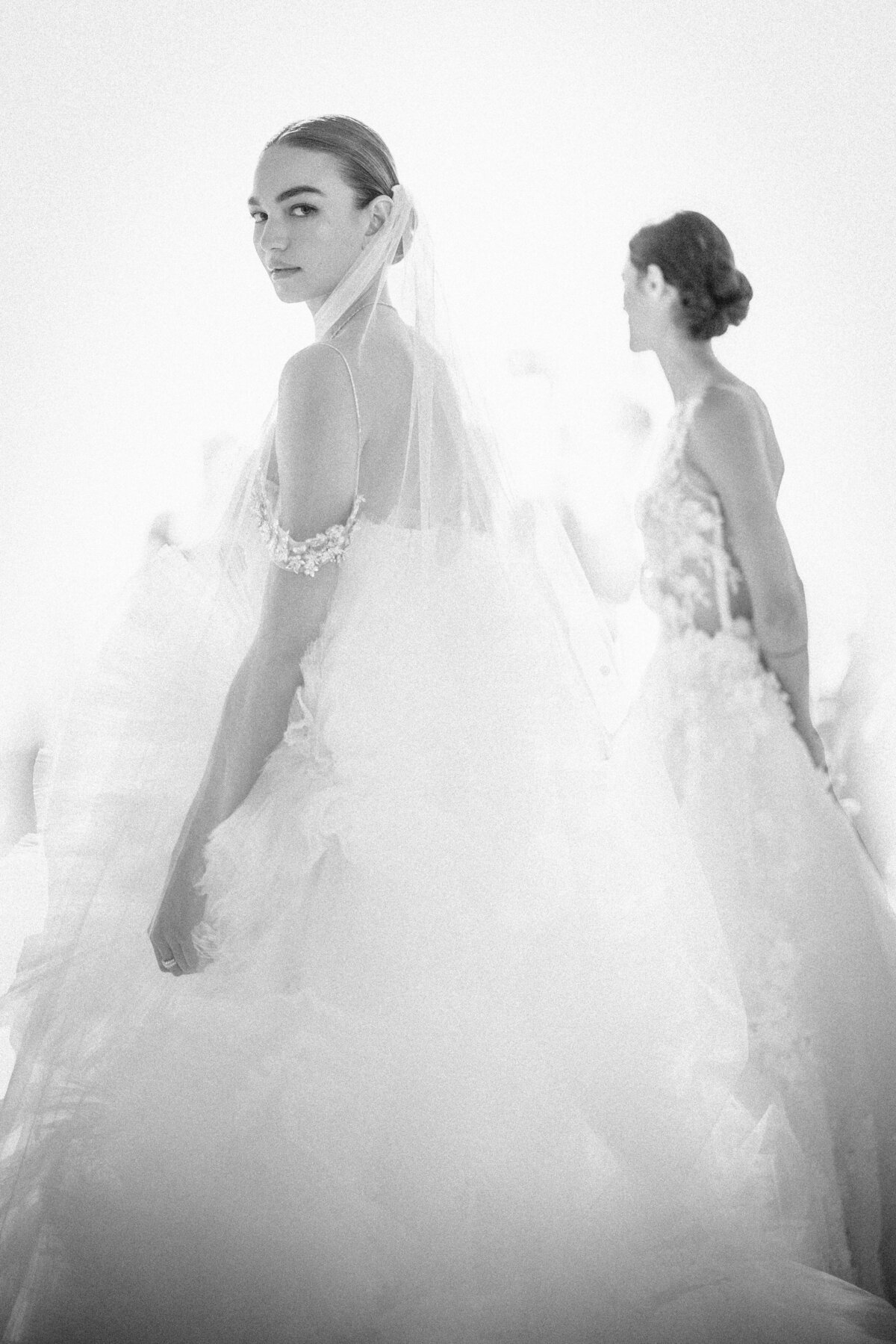 Two women in bridal gowns, one looking at the camera and the other facing away, in a softly lit setting at a New York Public Library wedding.
