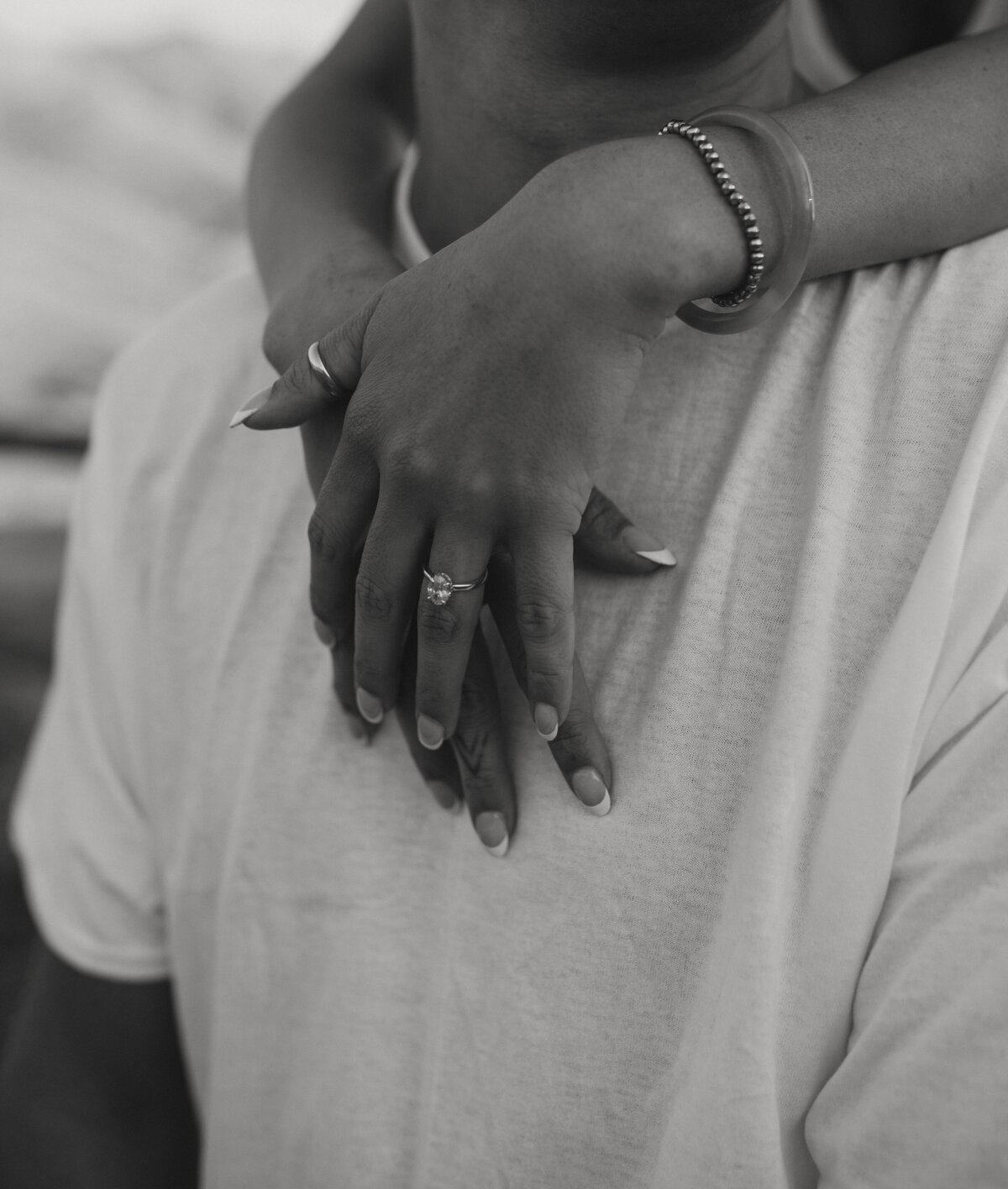 close up image of girl wrapping arms around boys neck engagement ring being shown off