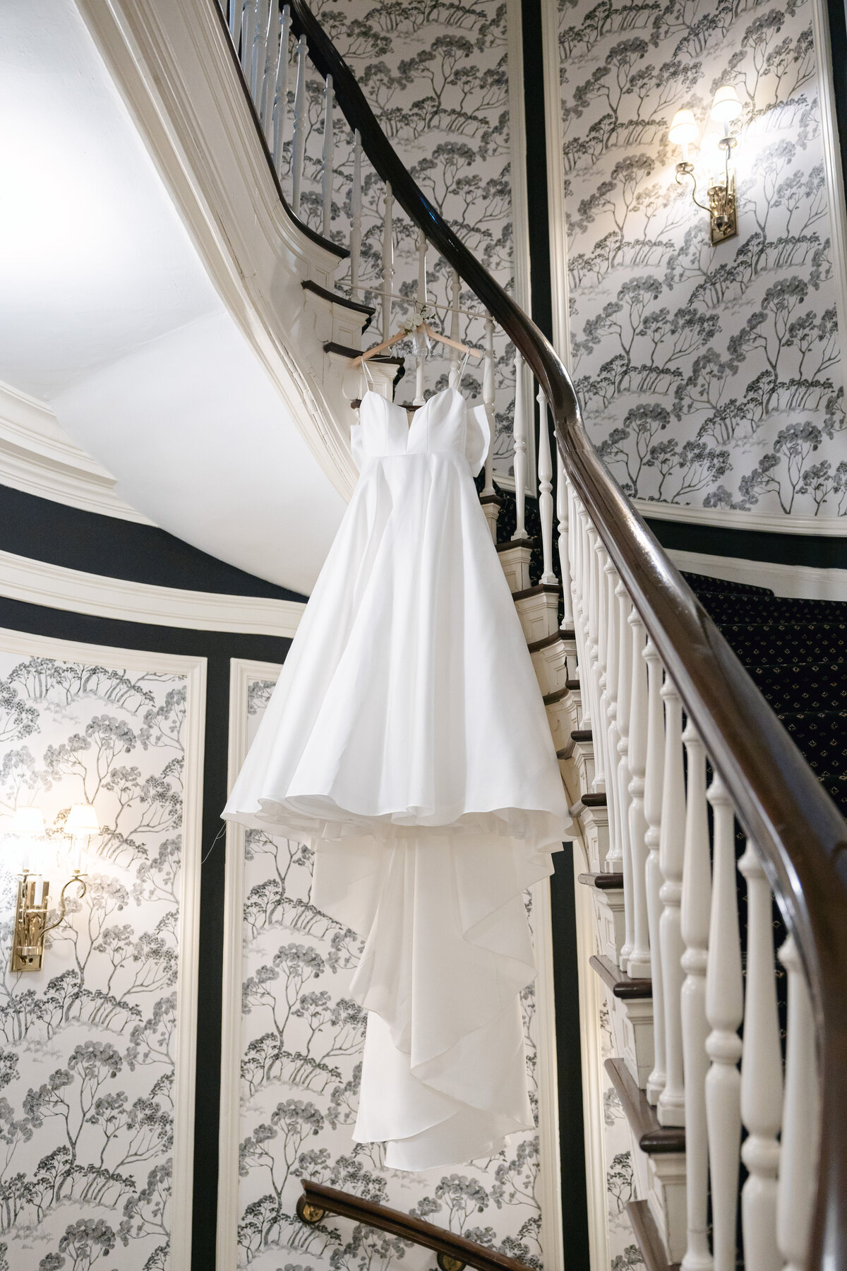 A stylish shot captured by a Madison wedding photographer of the bride's dress hanging elegantly from the stairs at The Madison Club in Madison, Wisconsin, highlighting the beauty and detail of the gown.