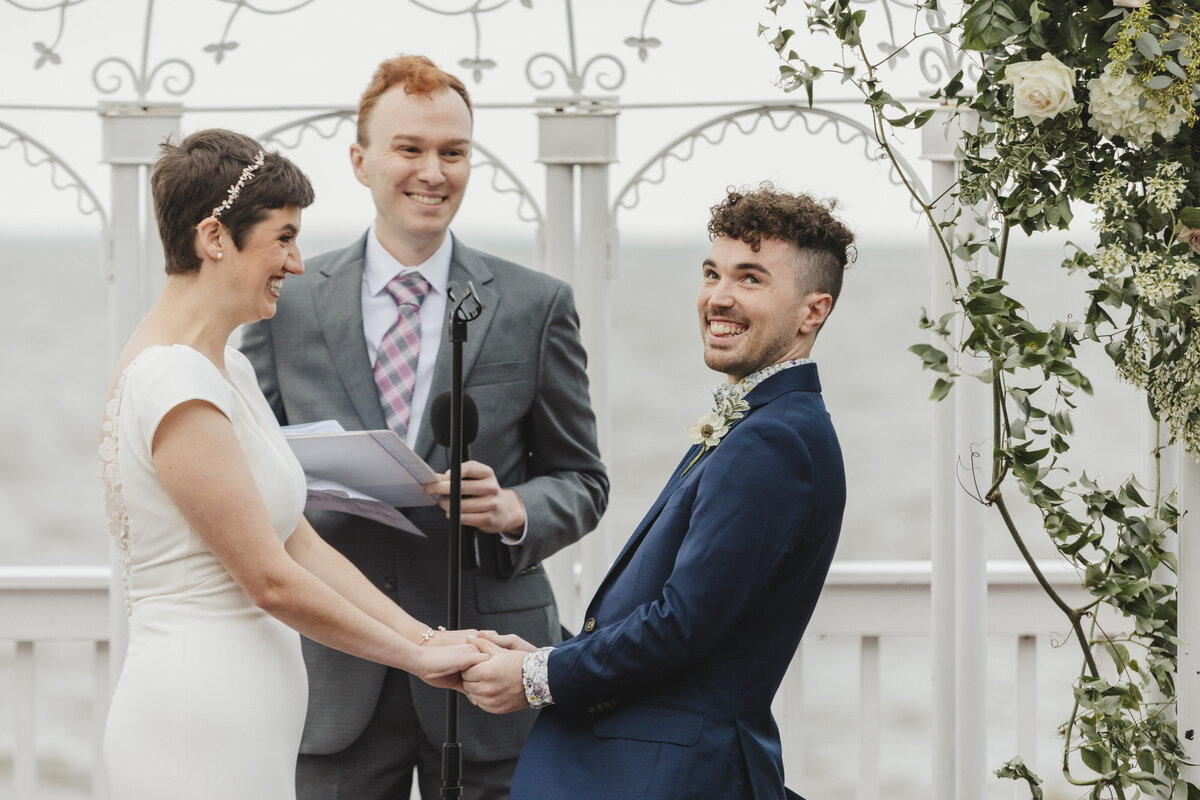 A wedding couple holding hands and smiling as they say their vows