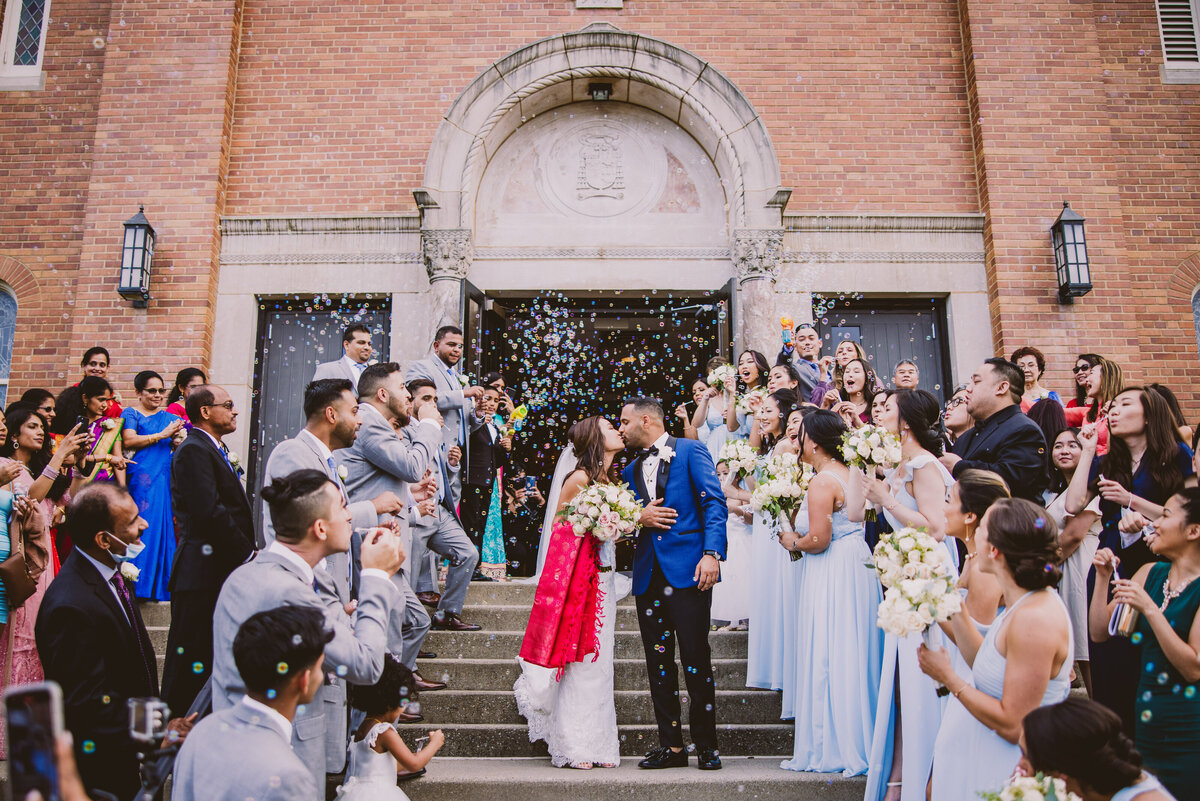 Indian christian bride and groom kissing outside the church steps during the bridal party bubble exit