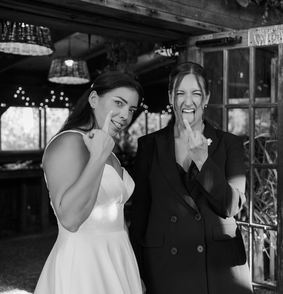 Black and white portrait of a bride and a guest laughing with their hands near their faces