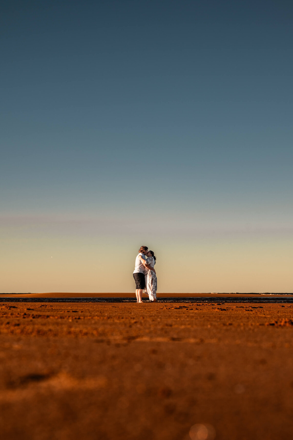 A couple embraces on a bright beach during the day, surrounded by sand and the sparkling ocean waves. - photo by Jamie Simmons