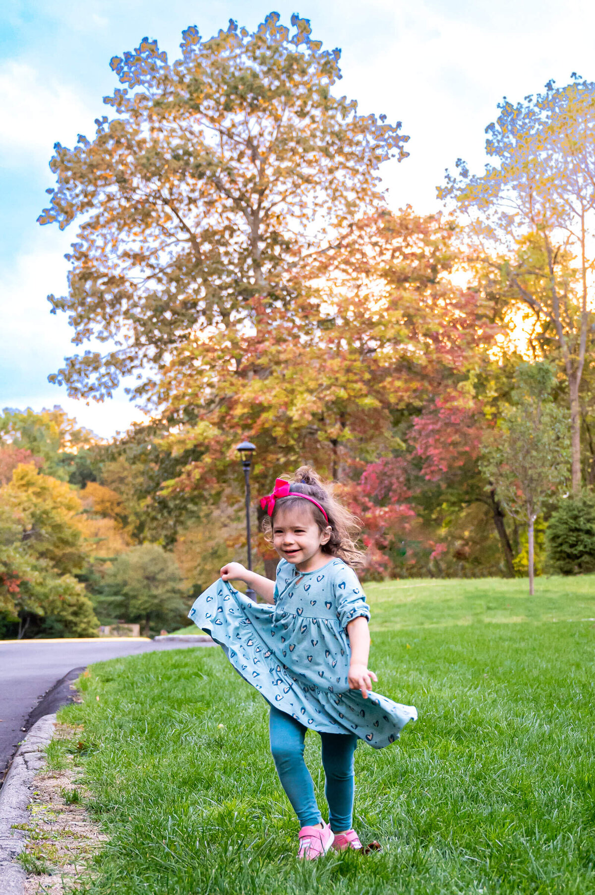 Toddler girl twirling while holding her dress as she dances outside in Westchester, NY.