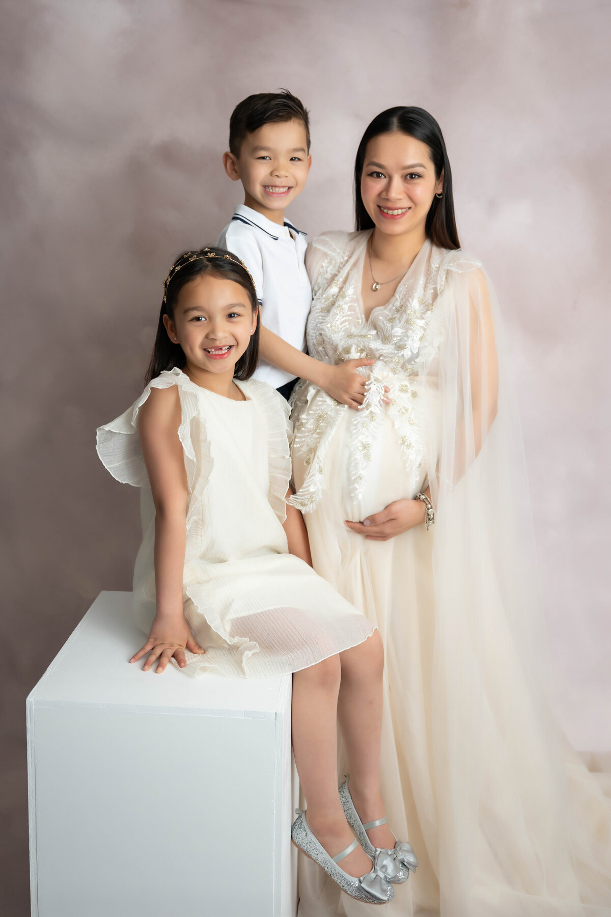 Two small children pose with pregnant mom while looking at the camera. 
