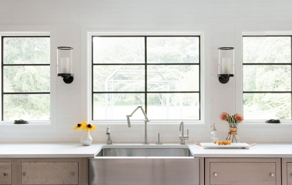 White oak kitchen cabinets with white counters and subway tile backsplash. New black Marvin windows frame a stunning garden view in the backyard.