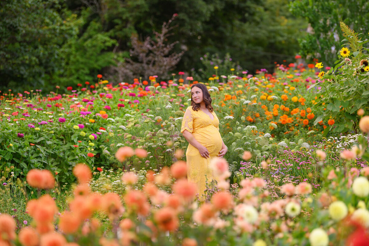pregnant woman wearing a yellow dress standing in a field of flowers for her outdoor maternity photos