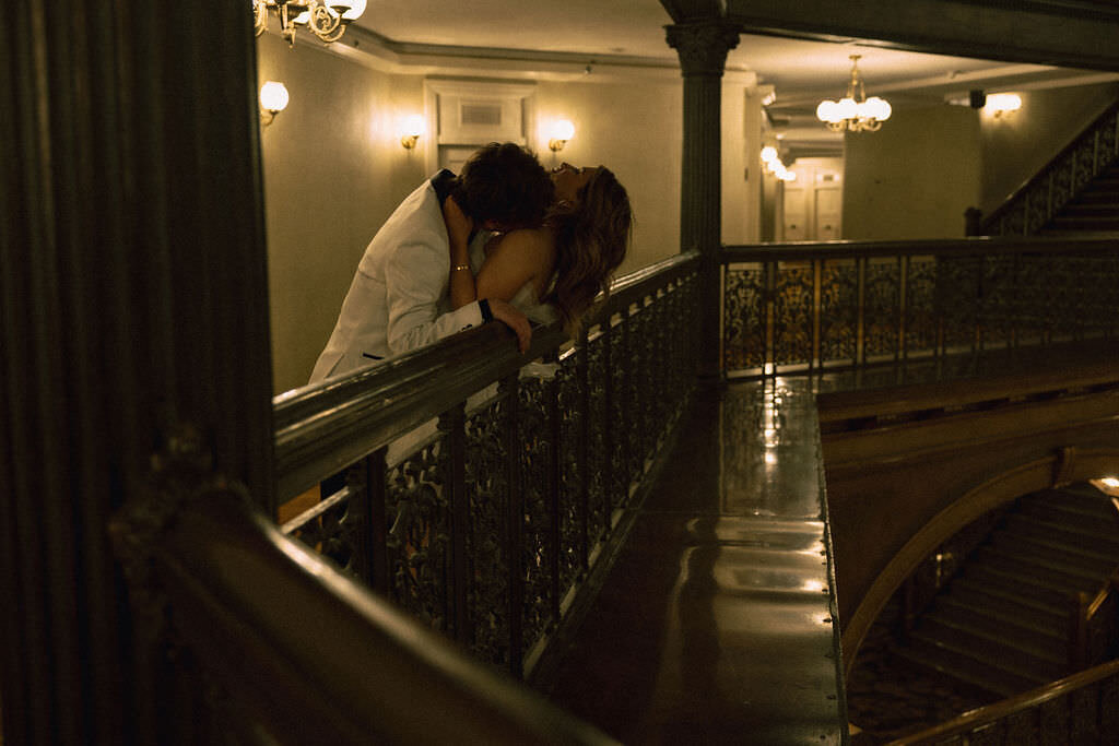 A couple kissing while leaning against a railing.