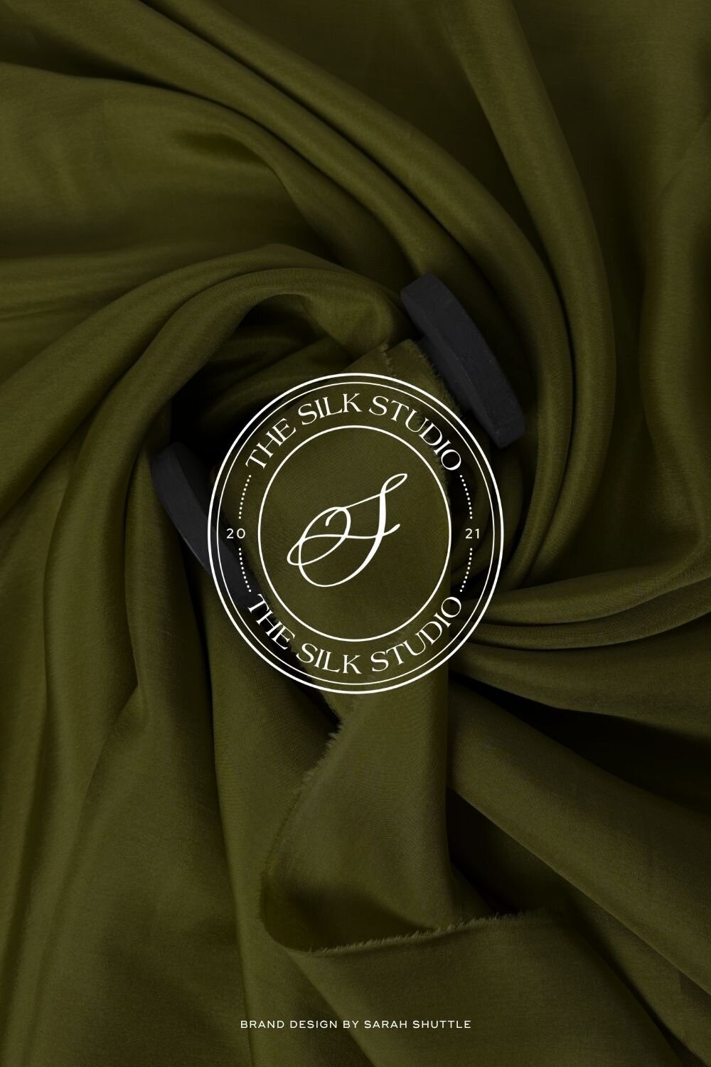 Oval brand submark for The Silk Studio placed on green silk fabric texture