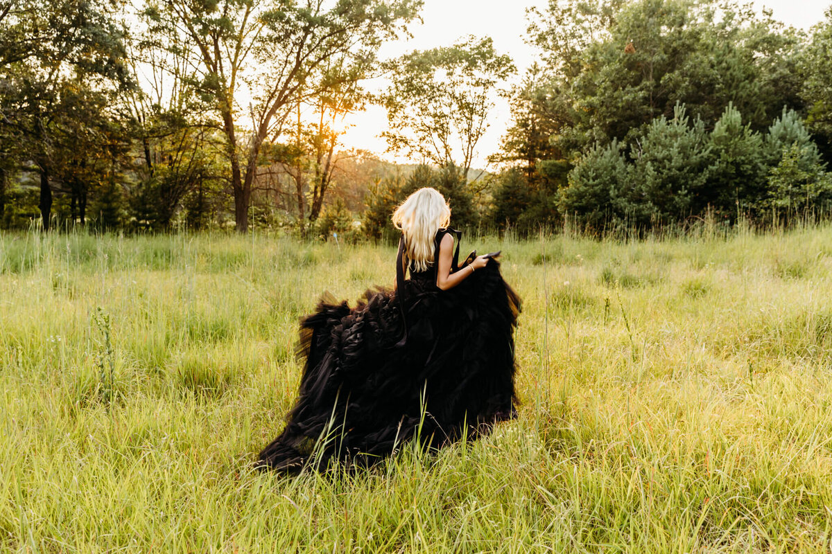 pretty teen girl in a tulle black dress running through the grassy field as she holds up her gown for her senior photography session.