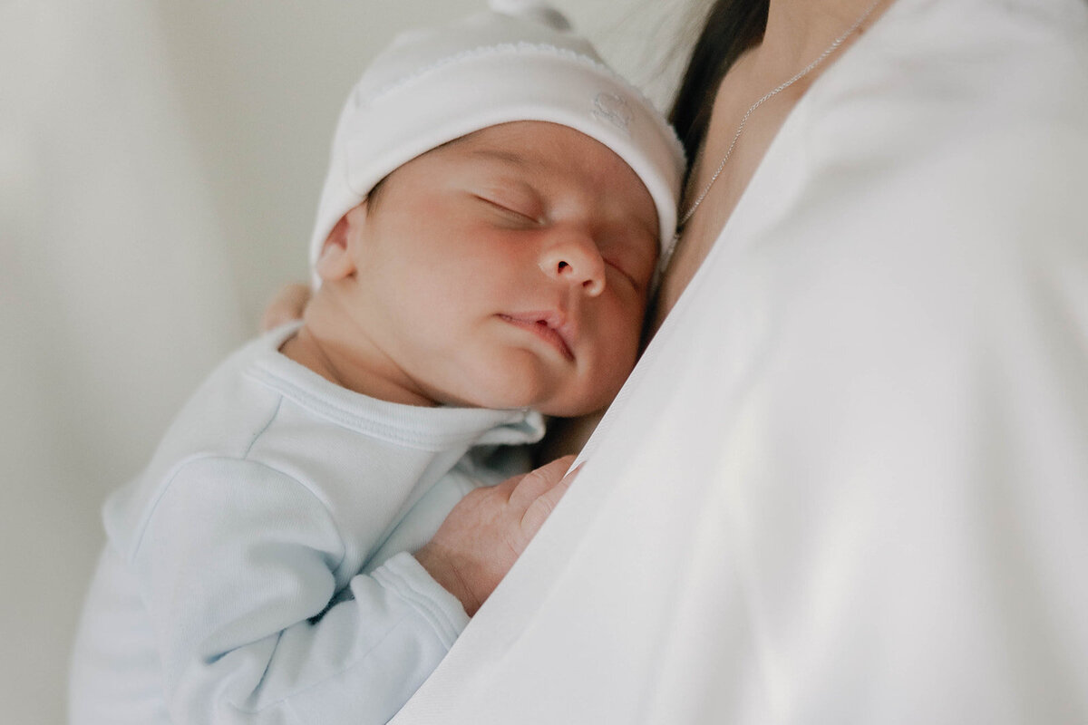 A peaceful newborn sleeps on their mother’s chest, dressed in soft pastel tones during a Florida Keys family session.