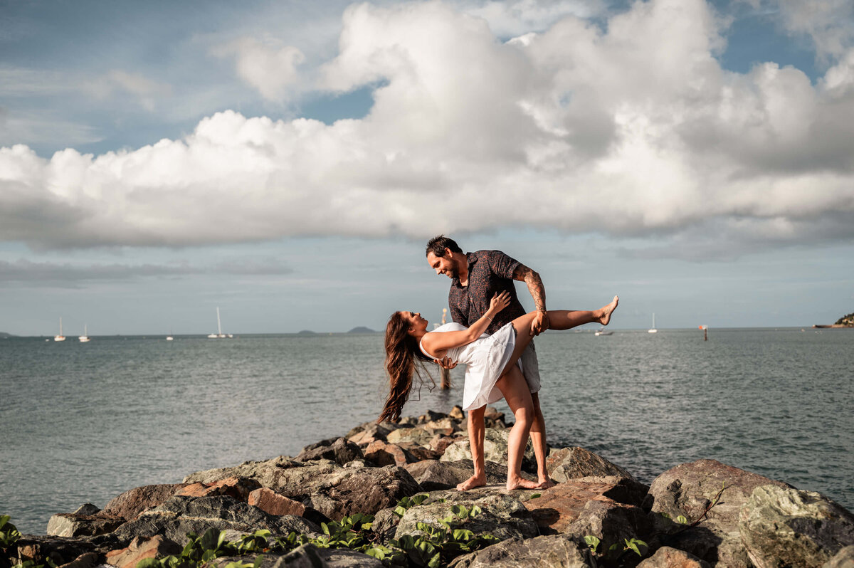 A man and woman stand on rocky terrain by the ocean, gazing at the waves and enjoying the coastal scenery - photo by Jamie SImmons