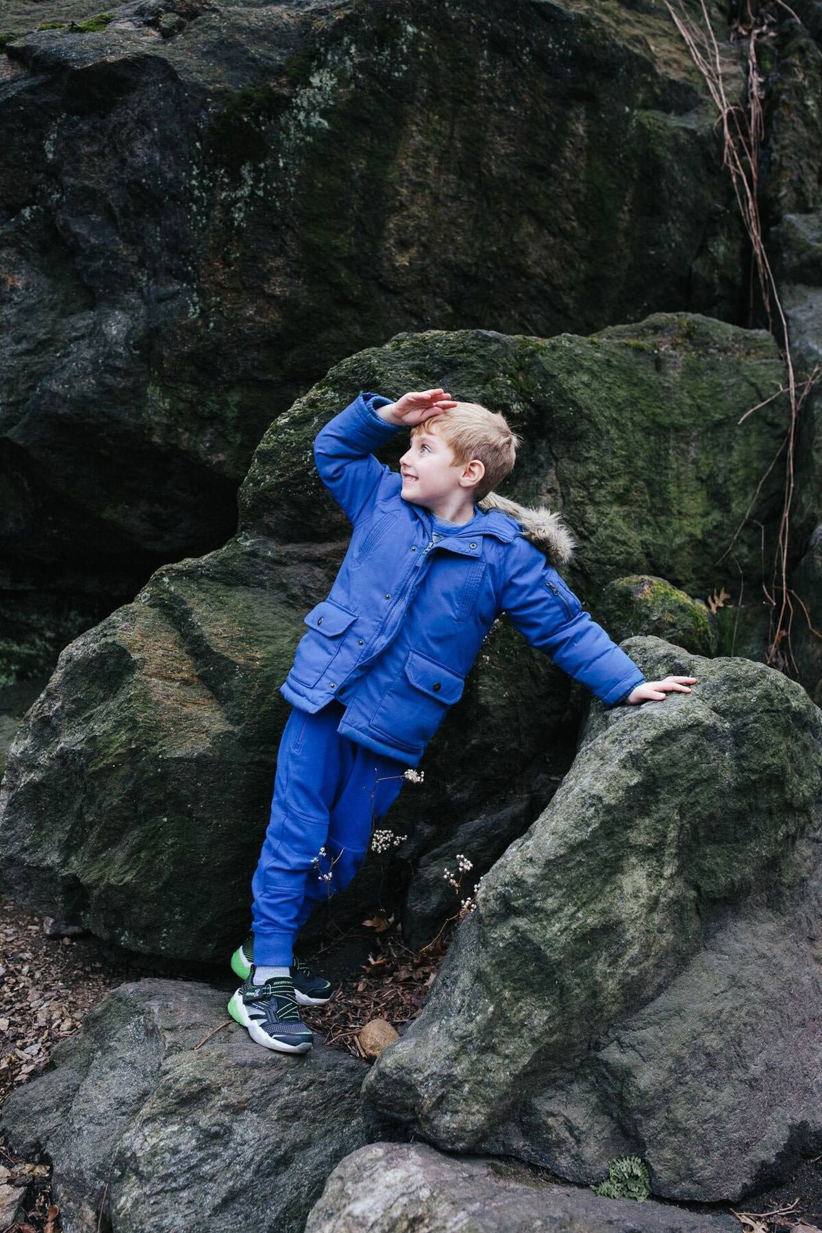boy wearing blue posing among the central park rocks in the winter