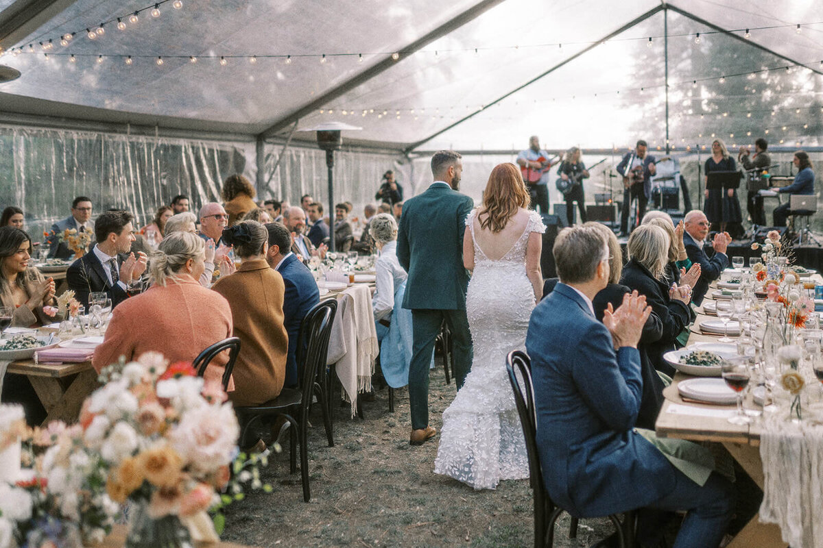 A bride and groom walking into a wedding reception tent facing away from the camera.