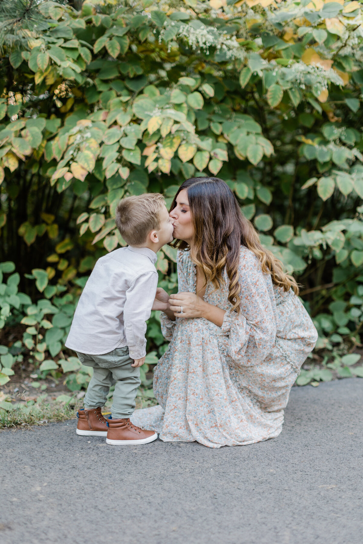 mom kissing her toddler son in front of lush greenery in a park photographed by Family Photographer South Jersey Tara Federico
