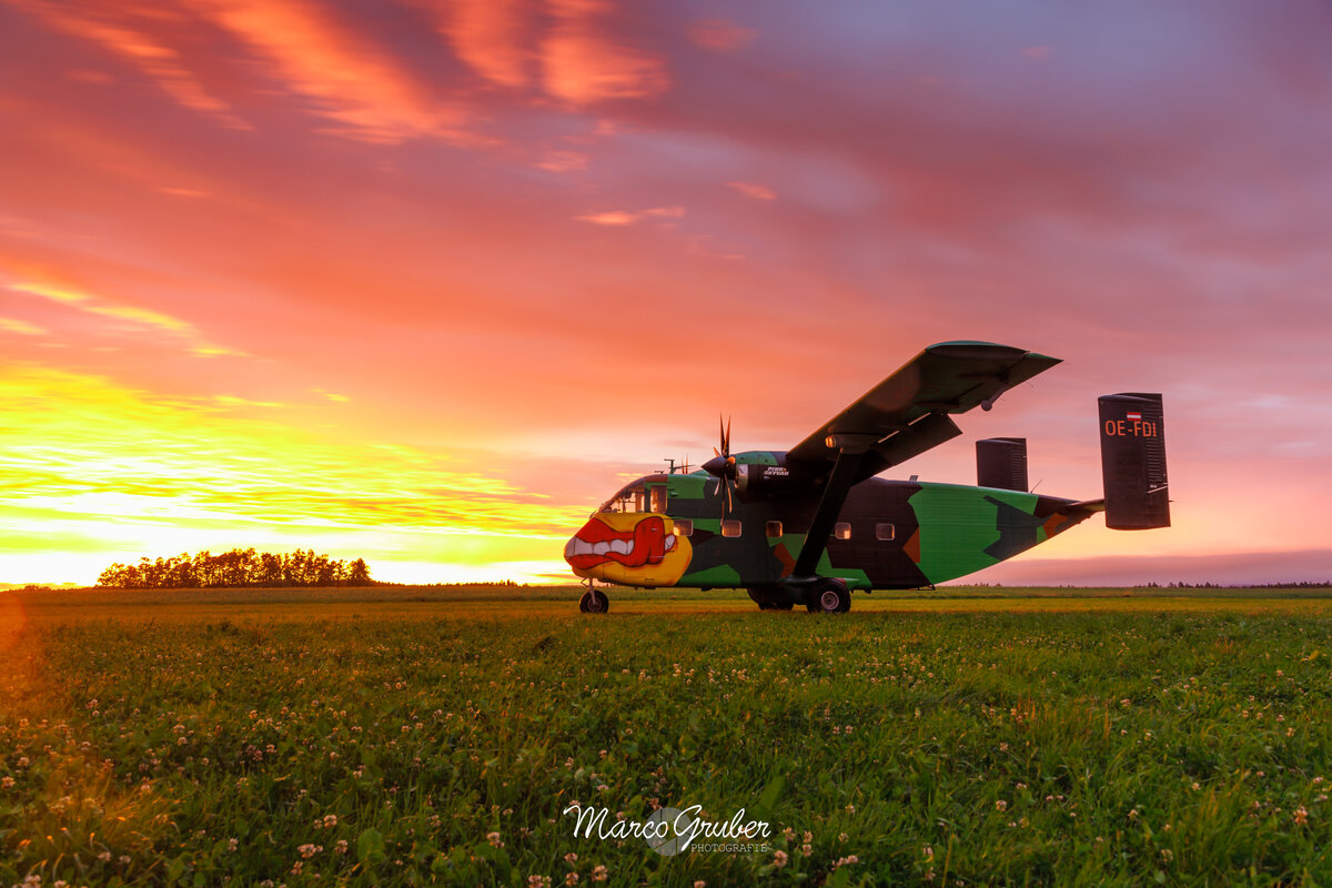 Die Pink Skyvan steht auf der grünen Wiese. Zu sehen ist ein wunderschöner Sonnenuntergang, der die Pink Skyvan anstrahlt